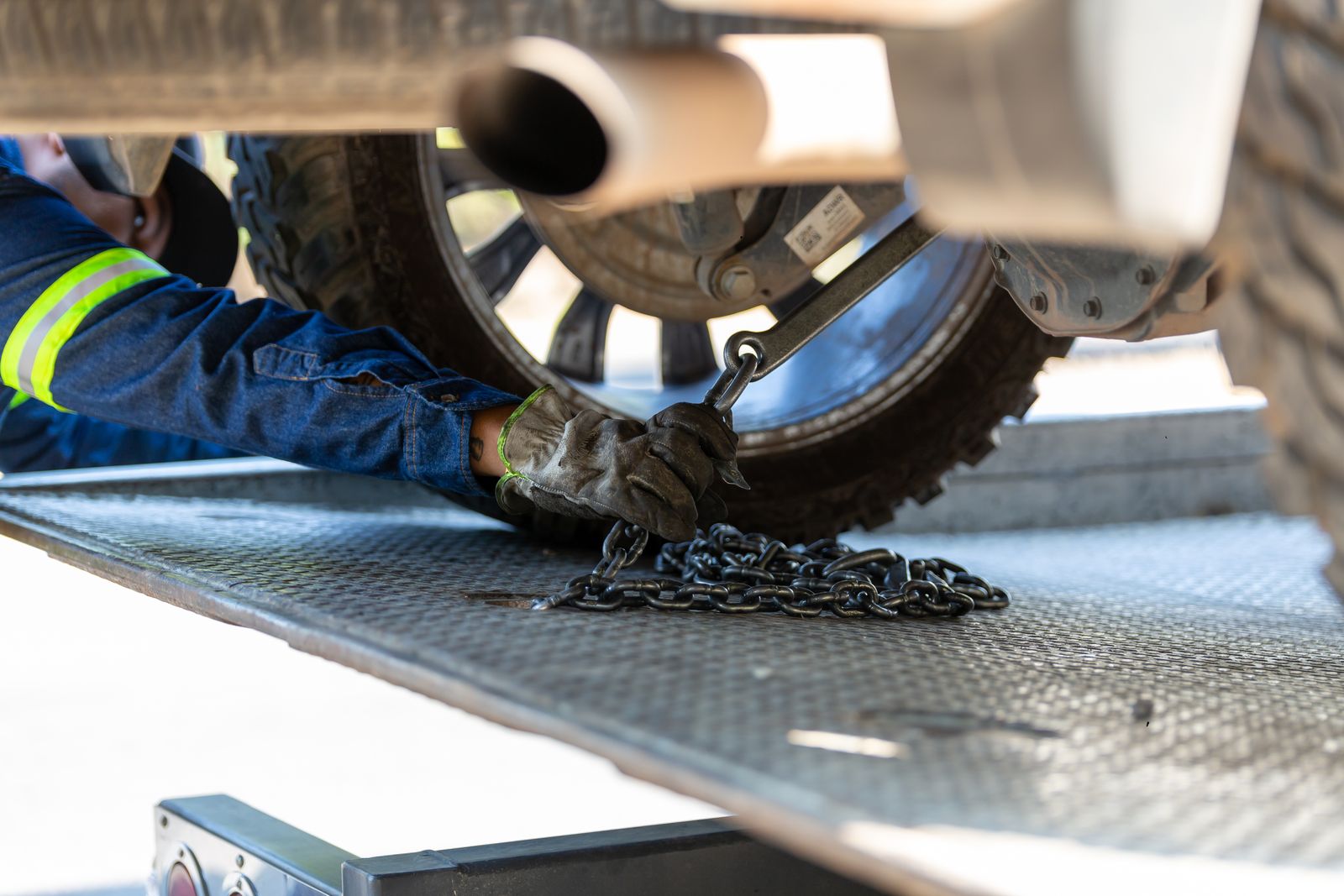A tow operator securing a vehicle's wheel with a chain on a flatbed